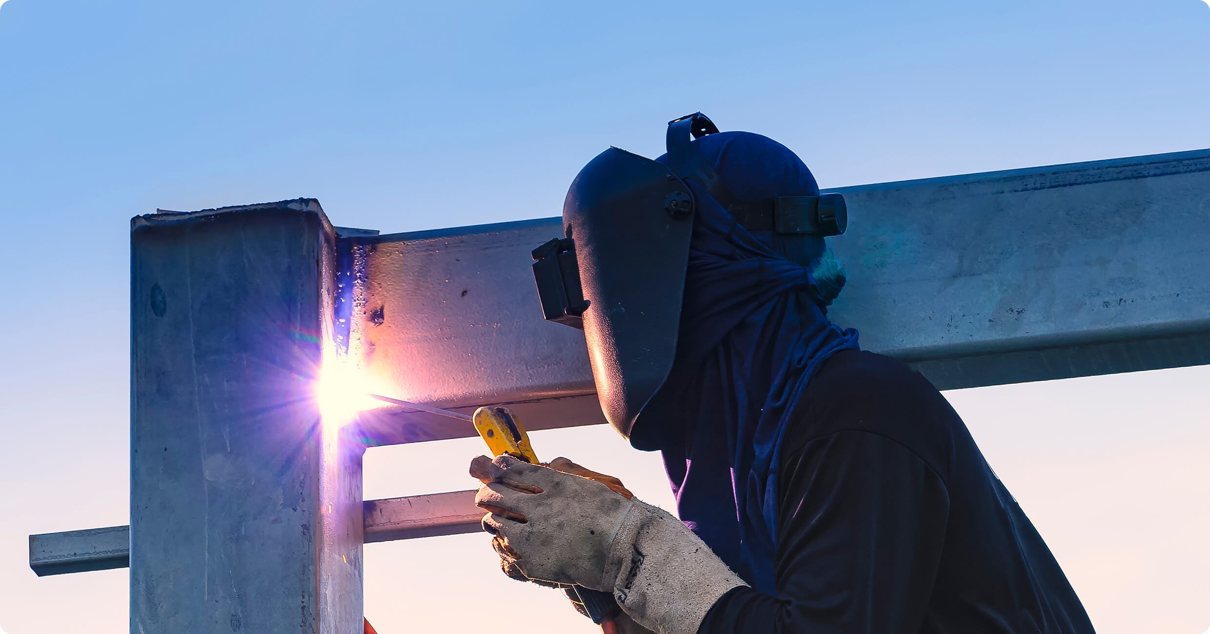 Welder working on metal structure outdoors.