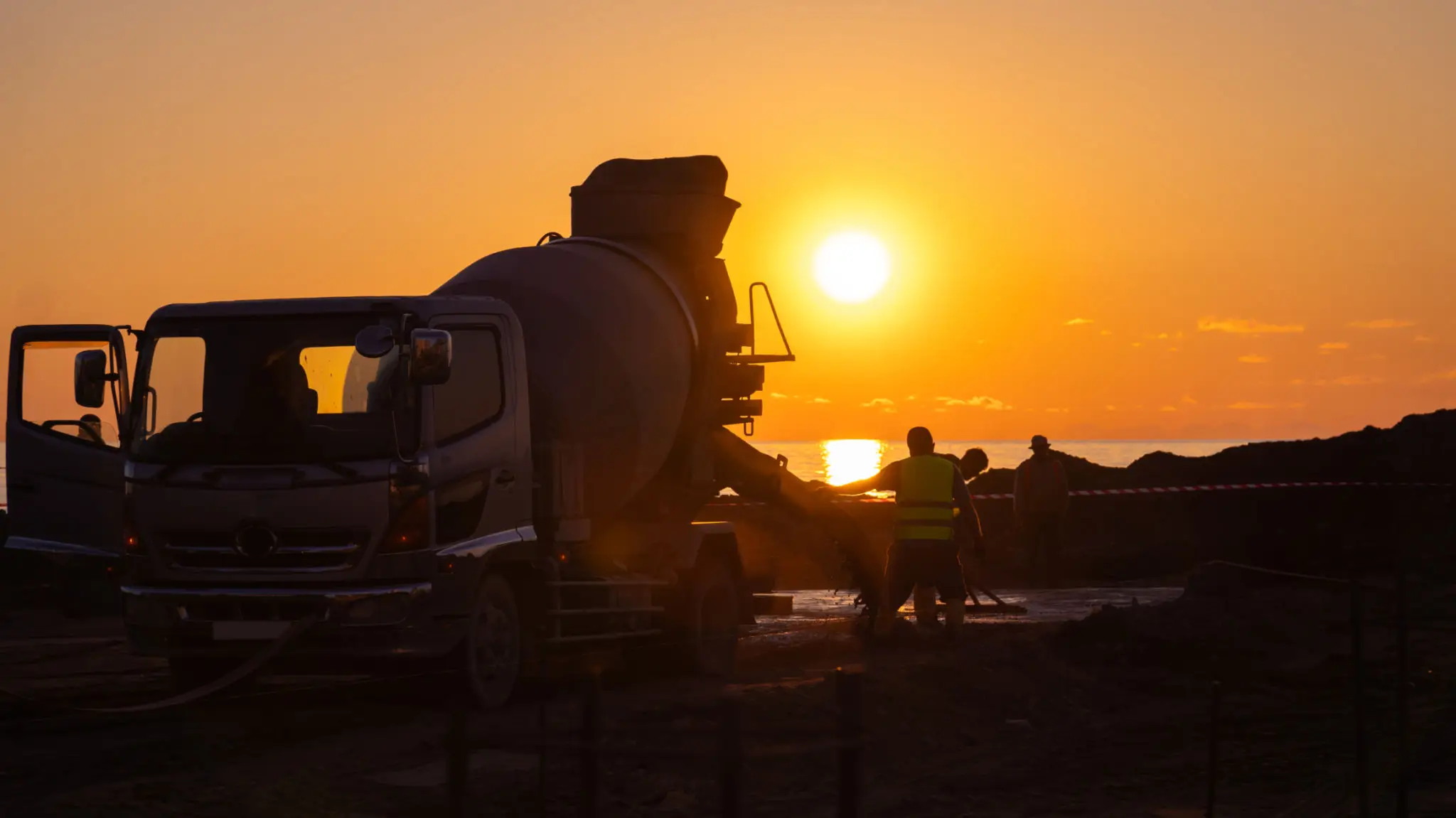 Silhouette of a person by a cement mixer at sunset on a construction site.