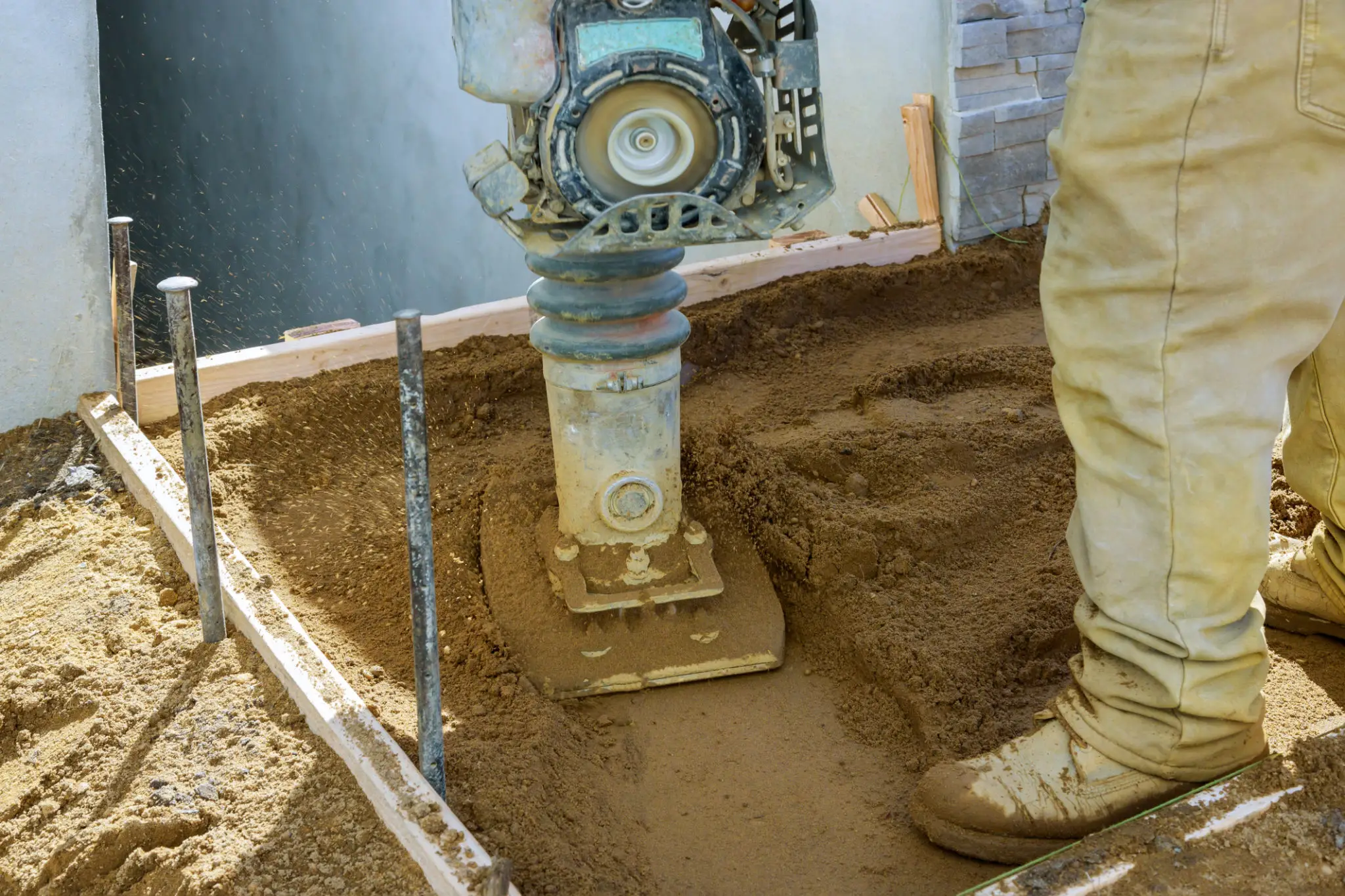 Worker using a compactor on a sand surface in a construction site.